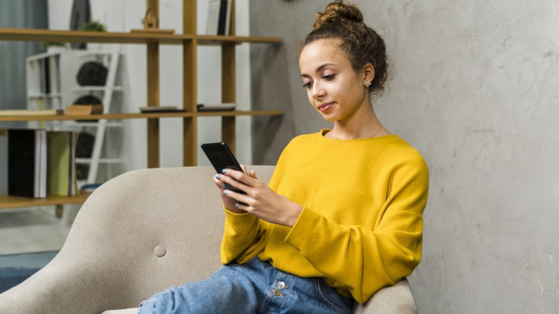 Девушка сидит в кресле и листает ленту в смартфоне на базе Android